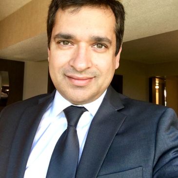 Man in a dark suit and tie smiling indoors.