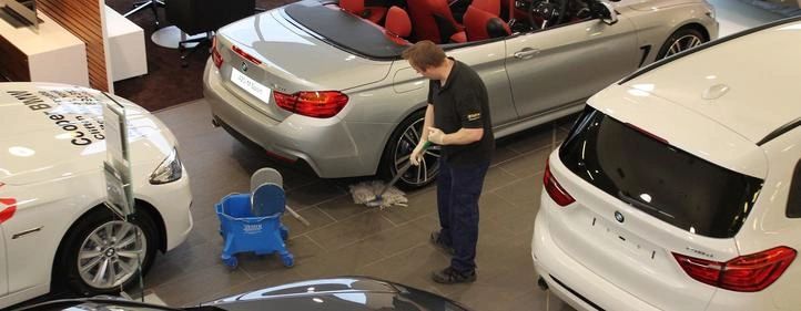 commercial cleaner mopping shiny floors between cars in a auto dealership showroom