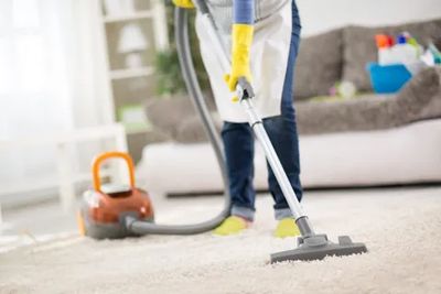cleaner vacuuming apartment carpets wearing yellow gloves and white uniform