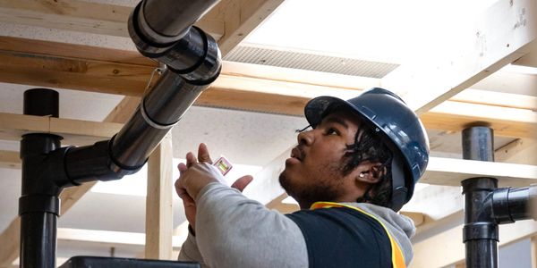 Plumber in a hard hat inspecting pipes with a level tool.