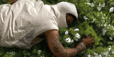Person lying on green plants with white flowers.