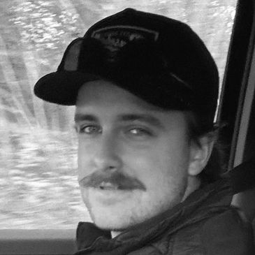 Man with mustache wearing a cap inside a vehicle.