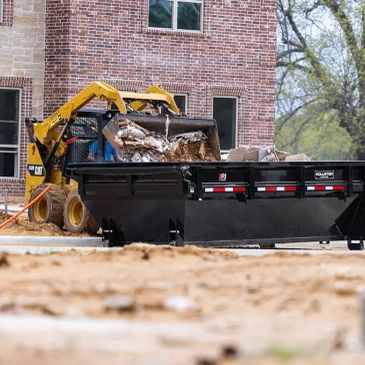 Yellow skid steer loader loading debris into a black dumpster.