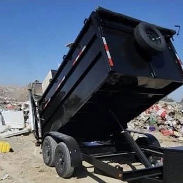Black dump trailer lifting its bed at a dumping site.