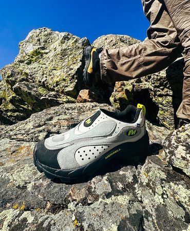 A hiking shoe placed on a rocky surface with a person standing nearby.