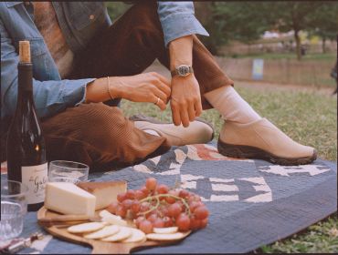 Person relaxing on a picnic blanket with wine and cheese platter.