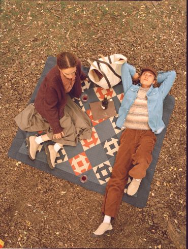 Two people relaxing on a patterned blanket outdoors in autumn.