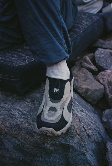 Person wearing unique sneakers sitting on rocks outdoors.