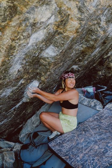 Woman bouldering on a rocky surface with climbing gear.