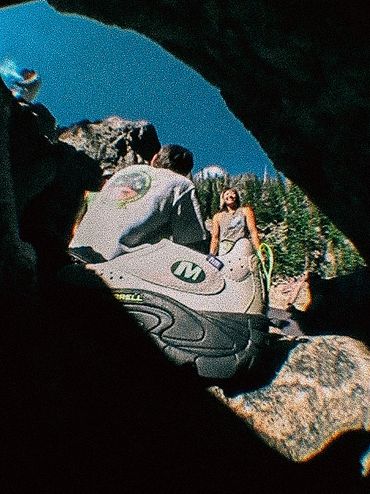 Two people in a rocky outdoor setting with one person sitting on a rock.