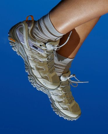 Close-up of legs wearing beige hiking shoes and socks against a blue background.