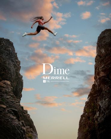 Person jumping across a rocky gap at sunset with Merrell branding.
