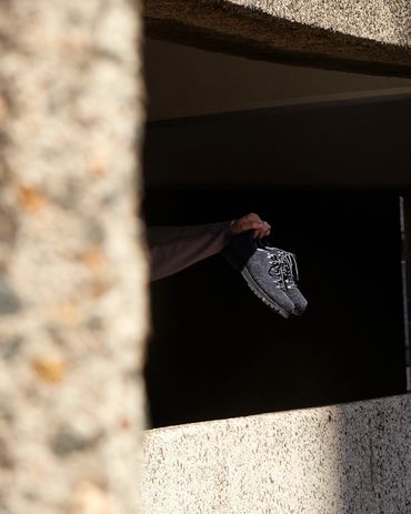 A hand holding a pair of black shoes against a dark background.