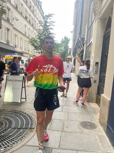Man in colorful shirt jogging on a city street with other people nearby.