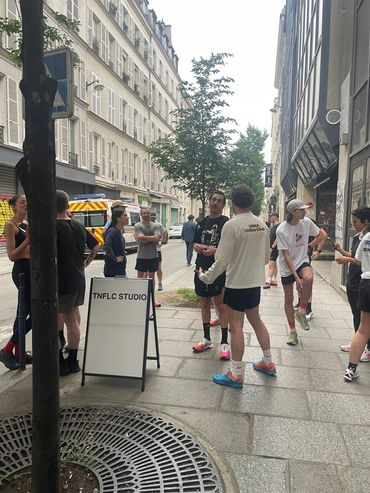 A group of people gathering near a sign for TNFLC Studio on a city sidewalk.