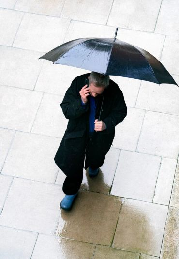 Person walking on wet pavement holding an umbrella and talking on phone.