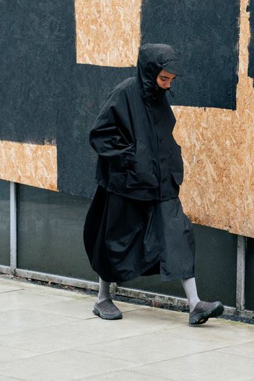 Person dressed in all-black walking on a sidewalk with head down.