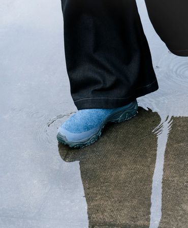 A person wearing blue shoes stepping into a puddle.