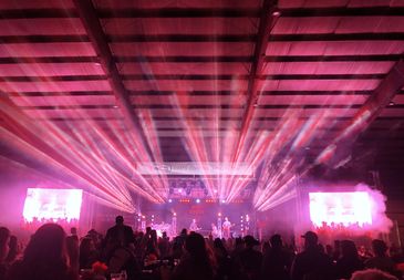 Indoor concert with vibrant pink and purple stage lights and a crowd enjoying the music.