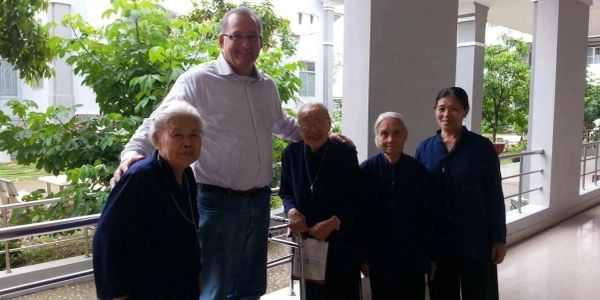A man posing with four elderly women outdoors.