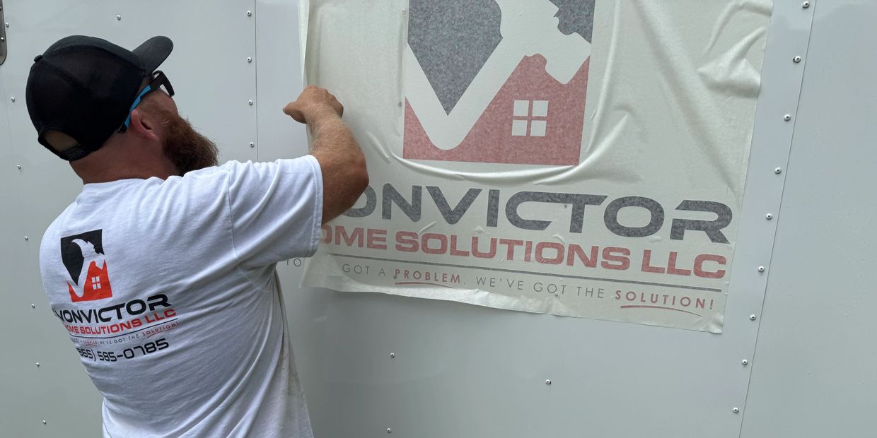 Man wearing Convictor Home Solutions LLC shirt applies a sign.