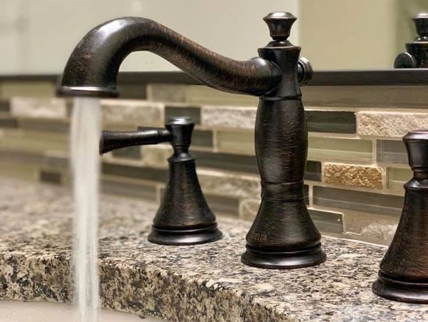Water flowing from a dark bronze faucet on a granite countertop.