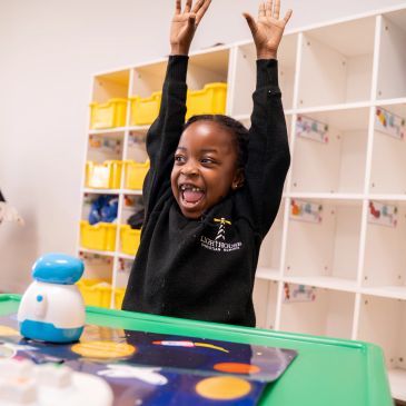 Excited girl raising hands at a table with educational robot toy.