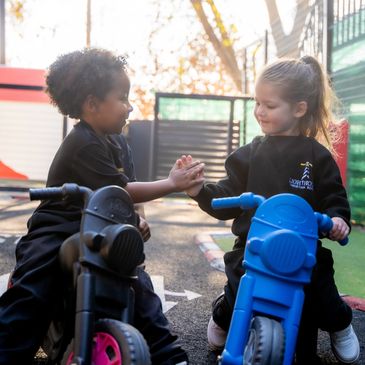 Two children playing on toy motorcycles outdoors.