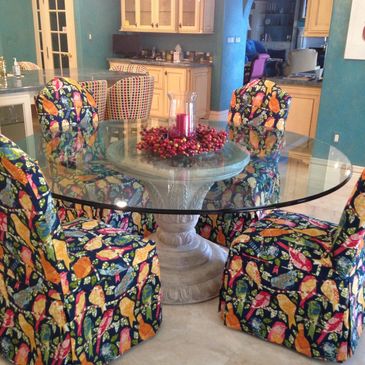 Colorful bird-patterned chairs surround a glass dining table with a festive centerpiece.