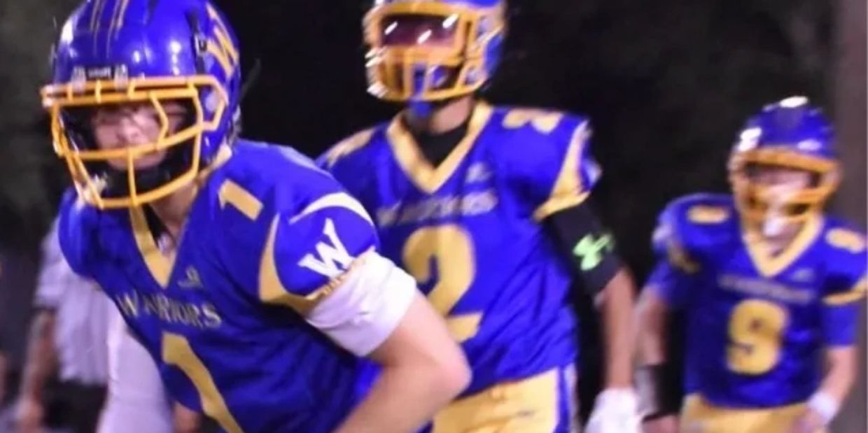 High school football players in blue and yellow uniforms during a night game.