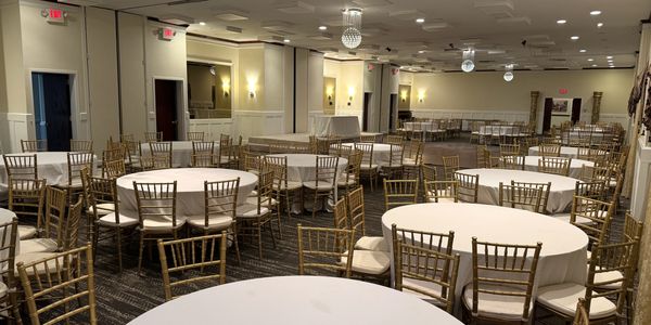 Elegant banquet hall with round tables and gold chairs.