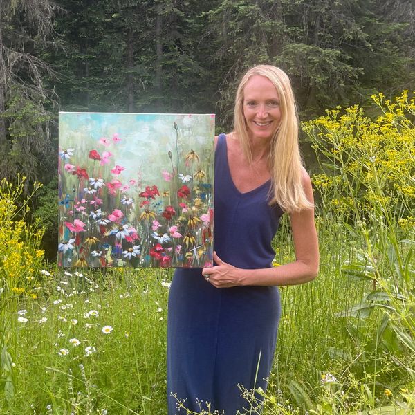 Woman holding a colorful flower painting in a garden.