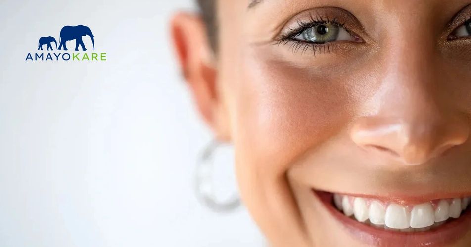 Close-up of a smiling woman with clear skin and blue eyes, accompanied by Amayokare logo.