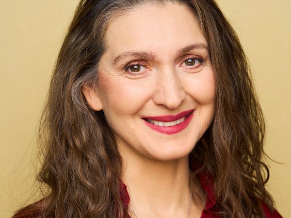 Smiling woman with long curly hair and warm makeup against a beige background.
