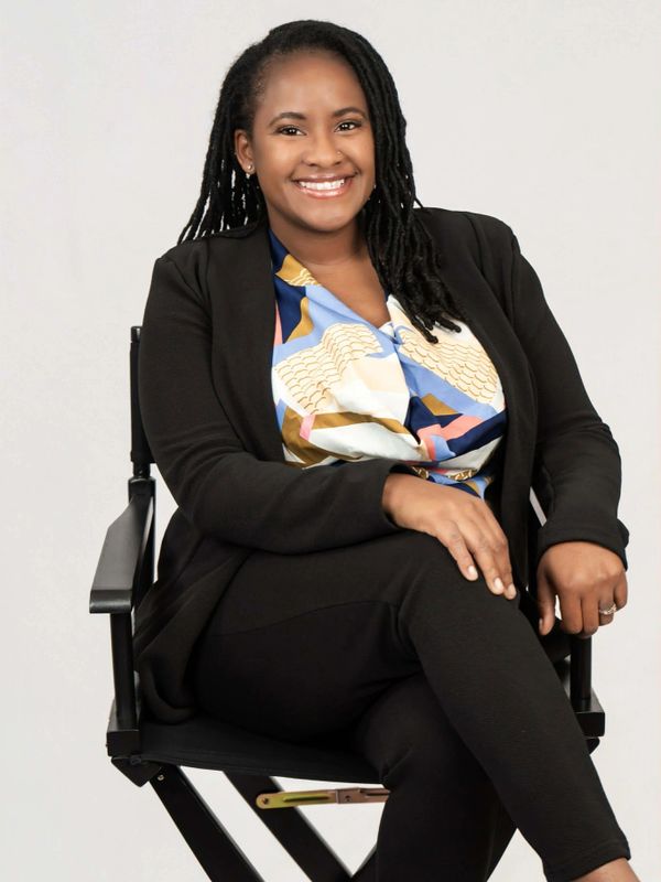 Smiling woman in a colorful blouse and black blazer seated confidently on a chair.