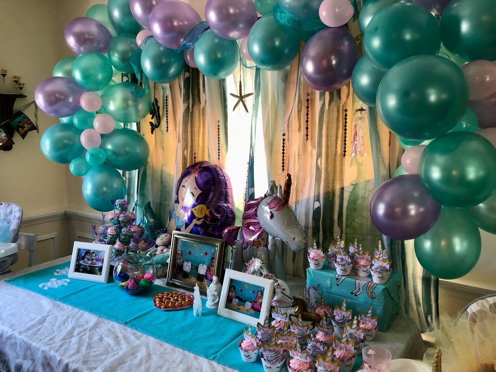 Balloon arch and table decorations using a theme of Mermaids and Unicorns in teal and purple.