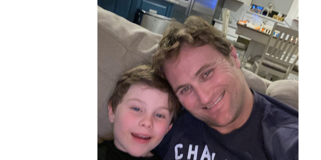 A smiling man and boy sitting closely on a couch at home.