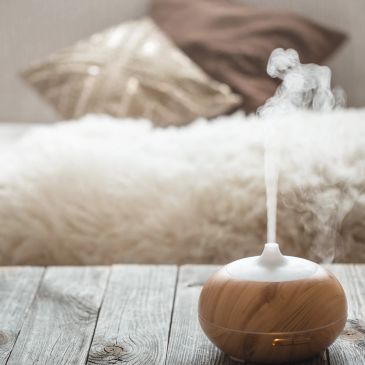 Wooden essential oil diffuser emitting mist on wooden table.