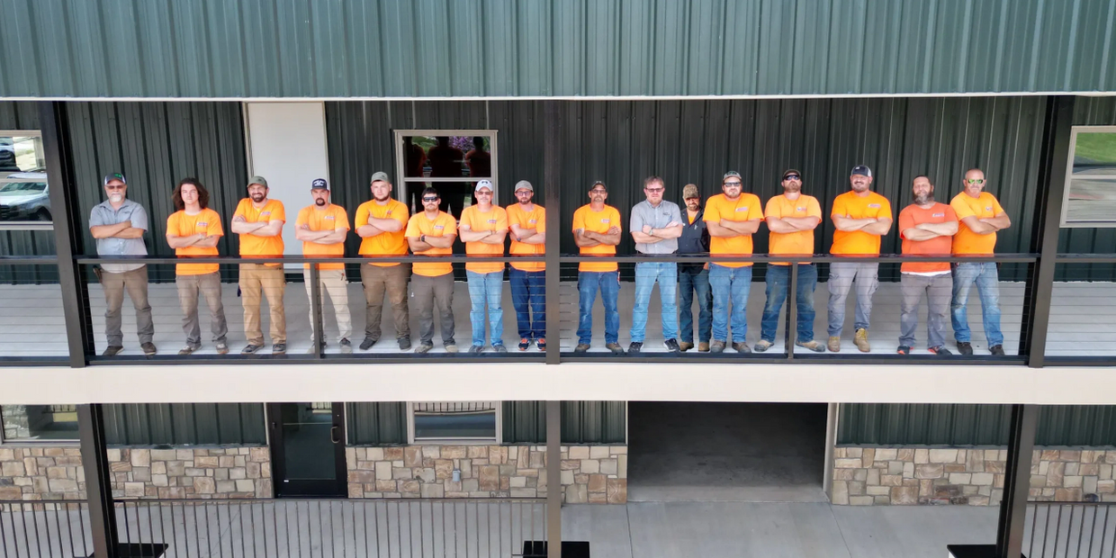 A group of people in orange shirts standing on a balcony with arms crossed.