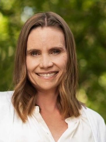 Smiling woman with shoulder-length brown hair outdoors.
