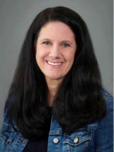 Woman with long black hair smiling in a denim jacket.