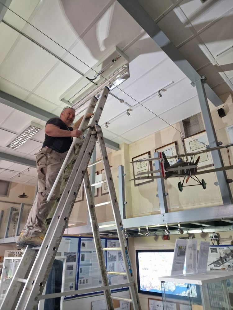 A man on a ladder installing or repairing a ceiling light in a museum-like setting.