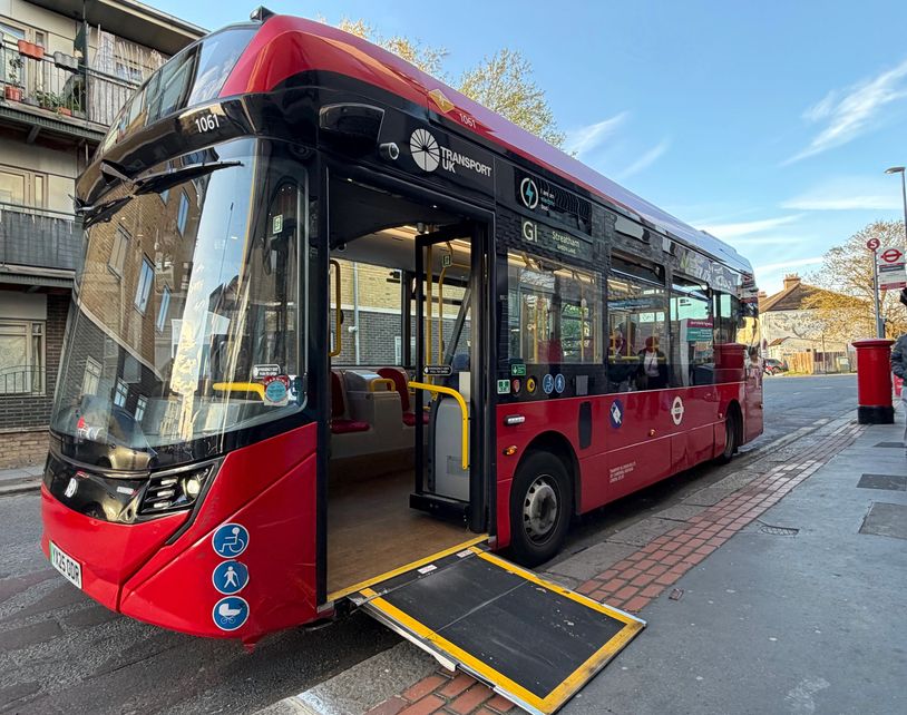 A single decker one door electric London bus at a bus stop with its ramp deployed at the front door.