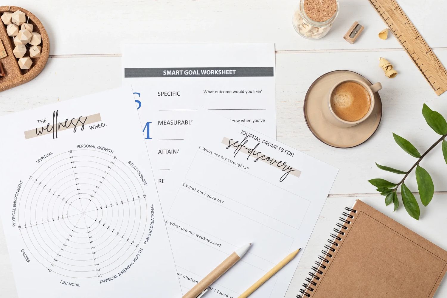 Wellness and self-discovery worksheets with coffee and stationery on a white desk.