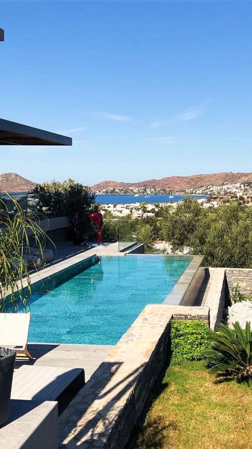 Infinity pool overlooking a coastal town with mountains and blue sky.