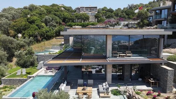 Modern multi-level house with pool and glass walls in a lush green area.