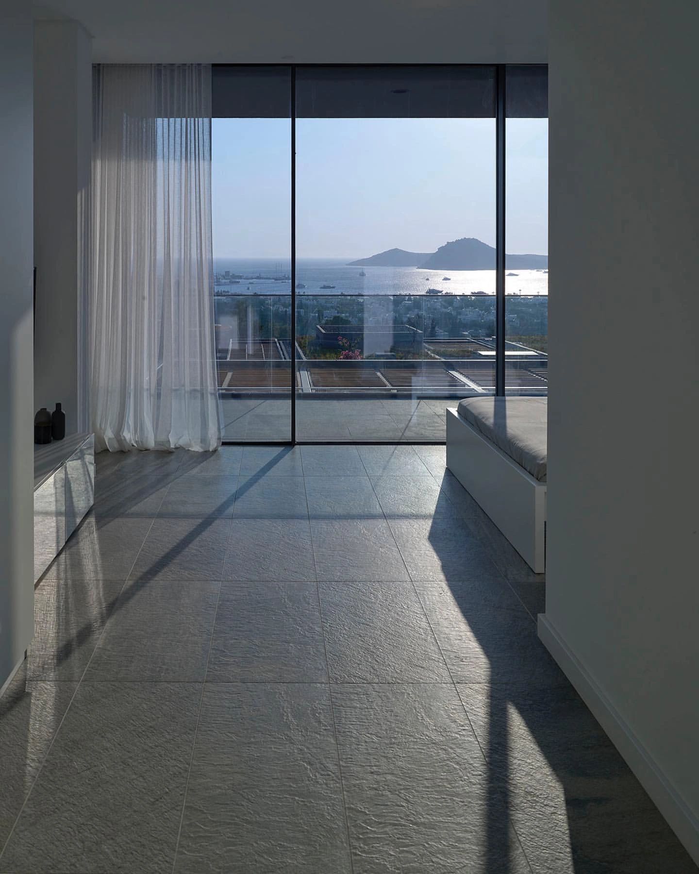 Minimalist room with large glass doors overlooking the sea and islands.