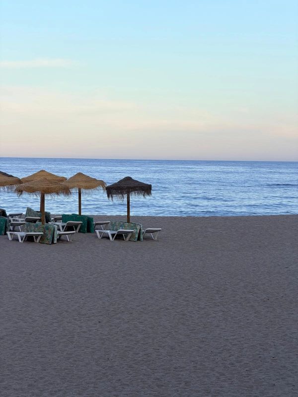 Empty beach chairs and umbrellas by the calm sea at dusk.