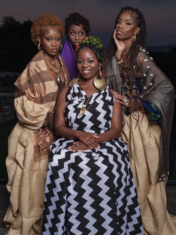 Four stylish women in vibrant, textured African-inspired attire pose confidently outdoors at dusk.