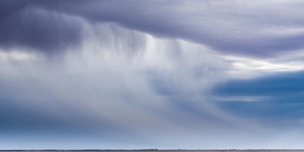 Rainfall seen from a distance under a cloudy sky.